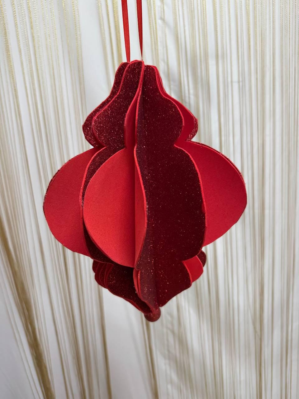 May include: A red, three-dimensional ornament with a glittery, textured surface. The ornament is suspended by a red ribbon. The design features layered, rounded shapes, creating a festive, decorative item. The ornament is suitable for holiday decor.