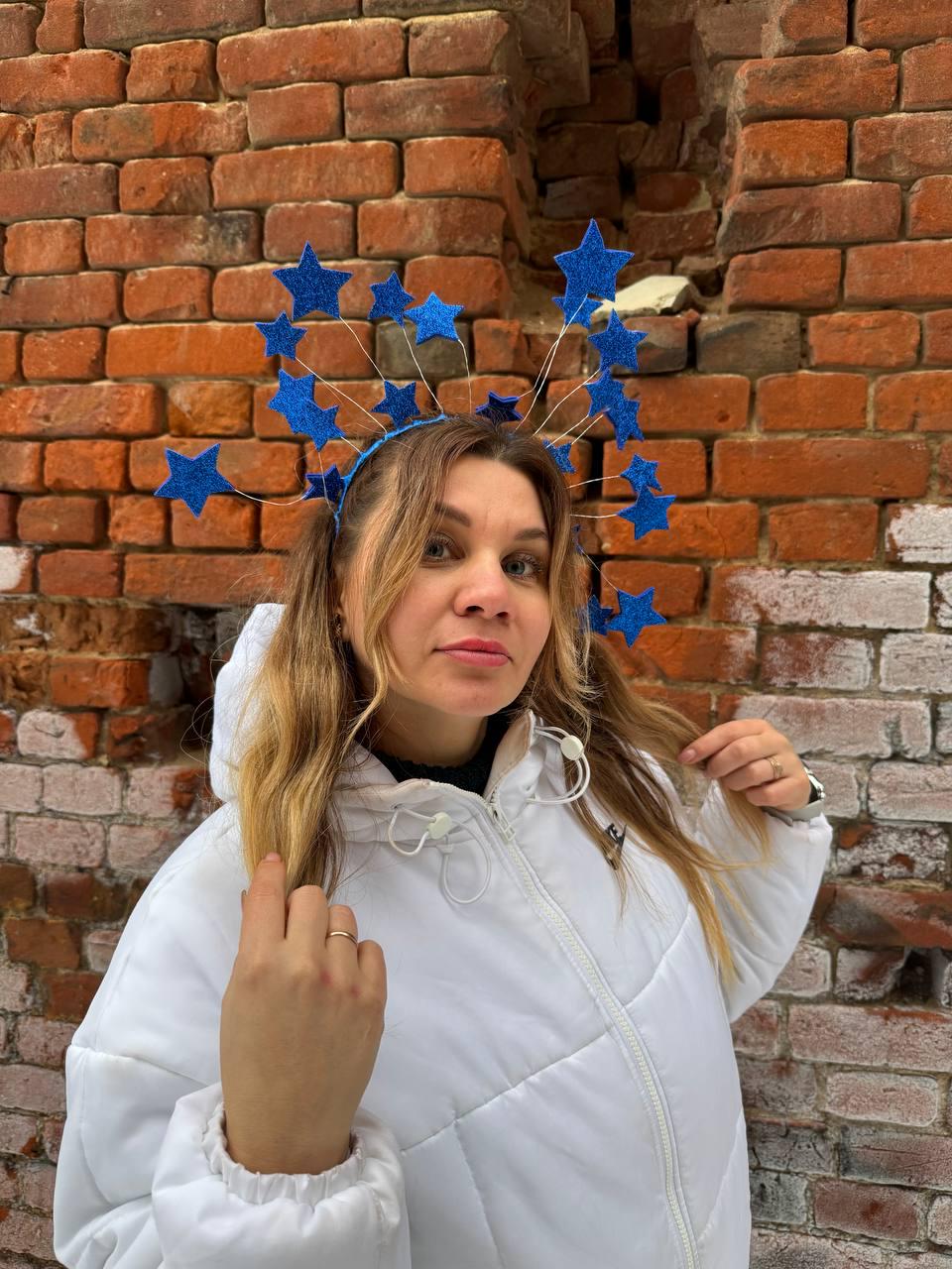 May include: A blue star headband with glittery accents. The headband features multiple star-shaped ornaments attached to thin wires, creating a celestial design. The stars are a vibrant blue color, and the headband is worn by a person wearing a white jacket.