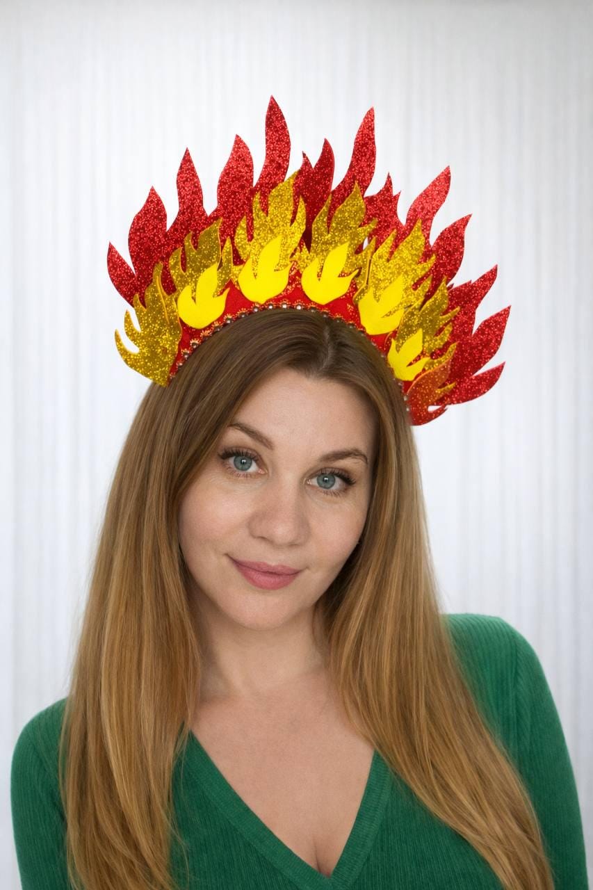 May include: A vibrant, handmade fire crown with red and yellow glittery flames. The crown is set on a red band with gold bead accents. Perfect for festivals, cosplay, or themed events. The crown is worn by a person with long blonde hair and a green shirt.