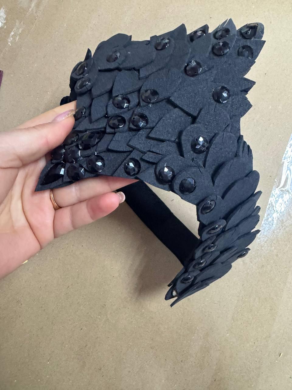 May include: Black headpiece with a layered, scale-like design. The headpiece is adorned with numerous black gemstones. The base is a black band. The headpiece is likely for costume or cosplay.