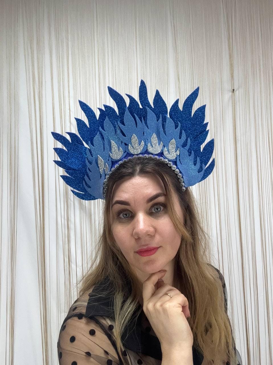 May include: A blue and silver glitter headdress with a flame design. The headpiece features a series of blue flame-shaped elements, with silver accents along the base. The headdress is designed to be worn on the head.