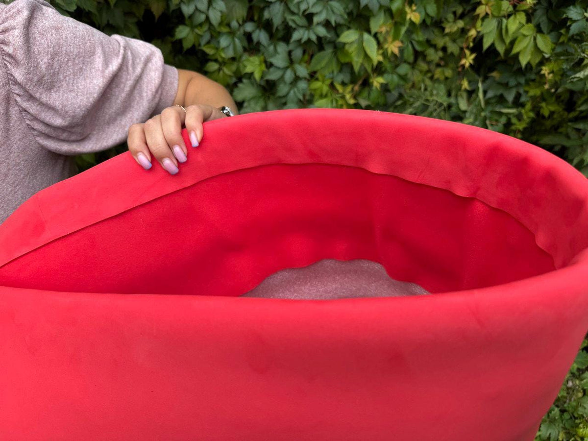 May include: A vibrant red, curved object with a soft, velvety texture. The interior is a lighter shade of red. The object is held by a person, with a green leafy background.