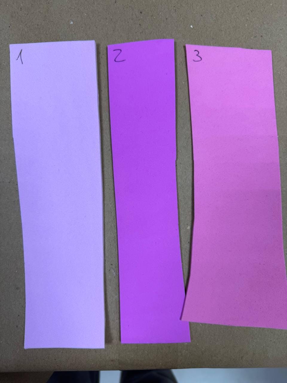 May include: Three rectangular paper strips arranged vertically. The first strip is light lavender and marked with the number 1. The second strip is a vibrant purple and marked with the number 2. The third strip is a bright pink and marked with the number 3.