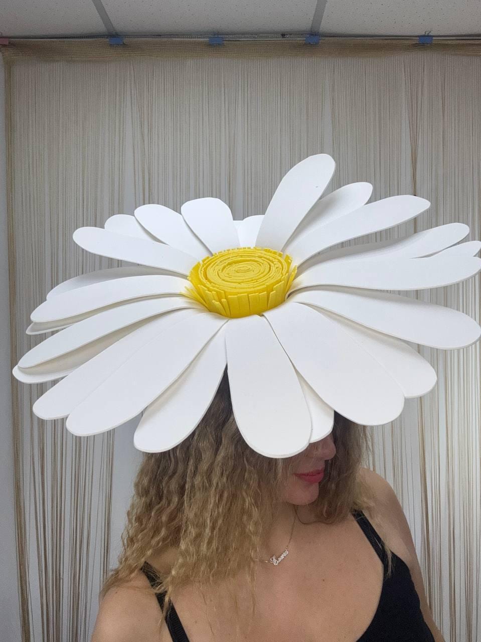 May include: A large, white daisy flower hat with a bright yellow center. The oversized petals are layered, creating a dimensional effect. The hat is a whimsical accessory, perfect for costumes or themed events.