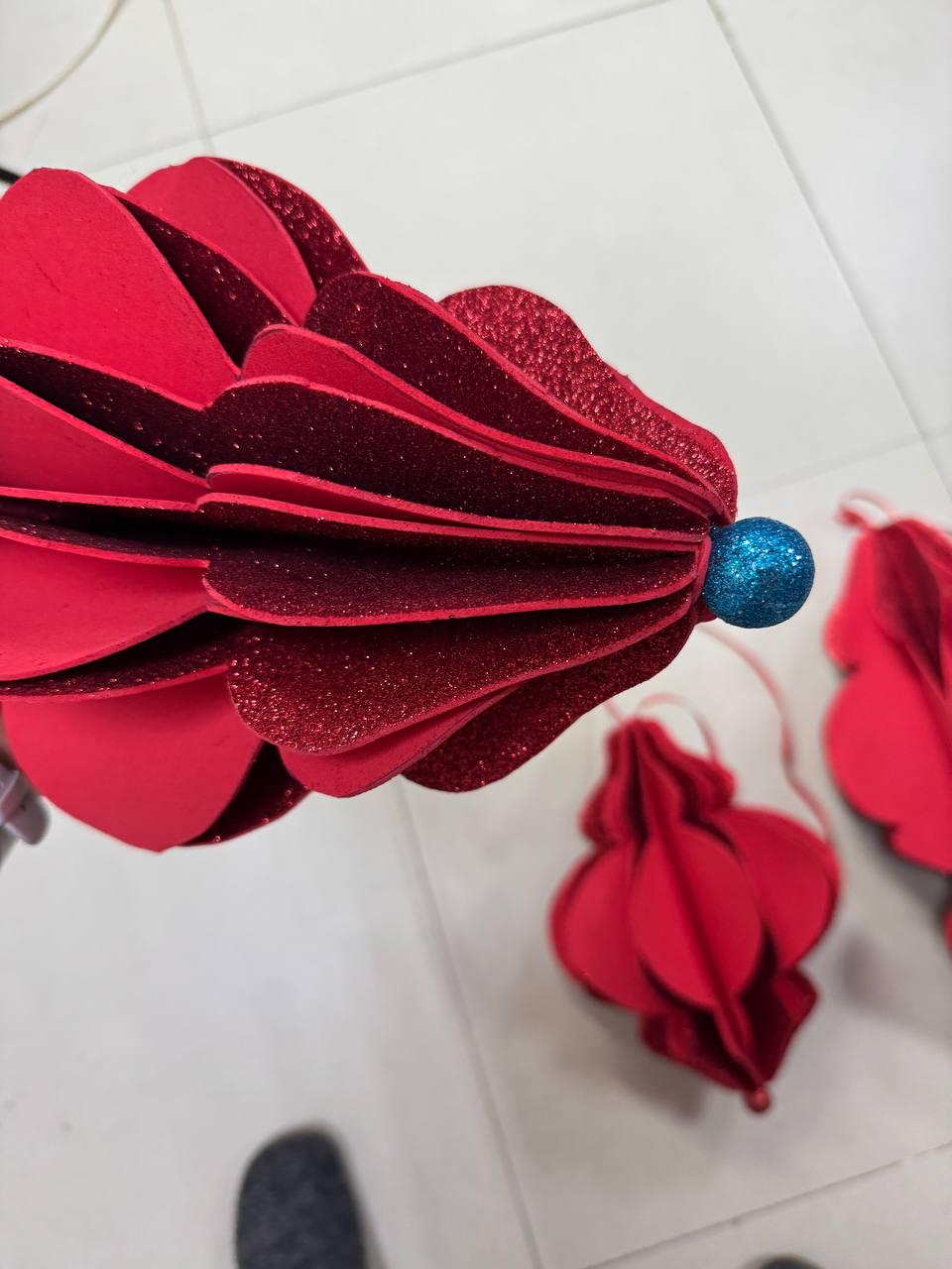 May include: Red paper ornaments with a layered design and glitter accents. Each ornament has a blue glitter ball at the center and a string for hanging. The ornaments are likely for holiday or festive decor.