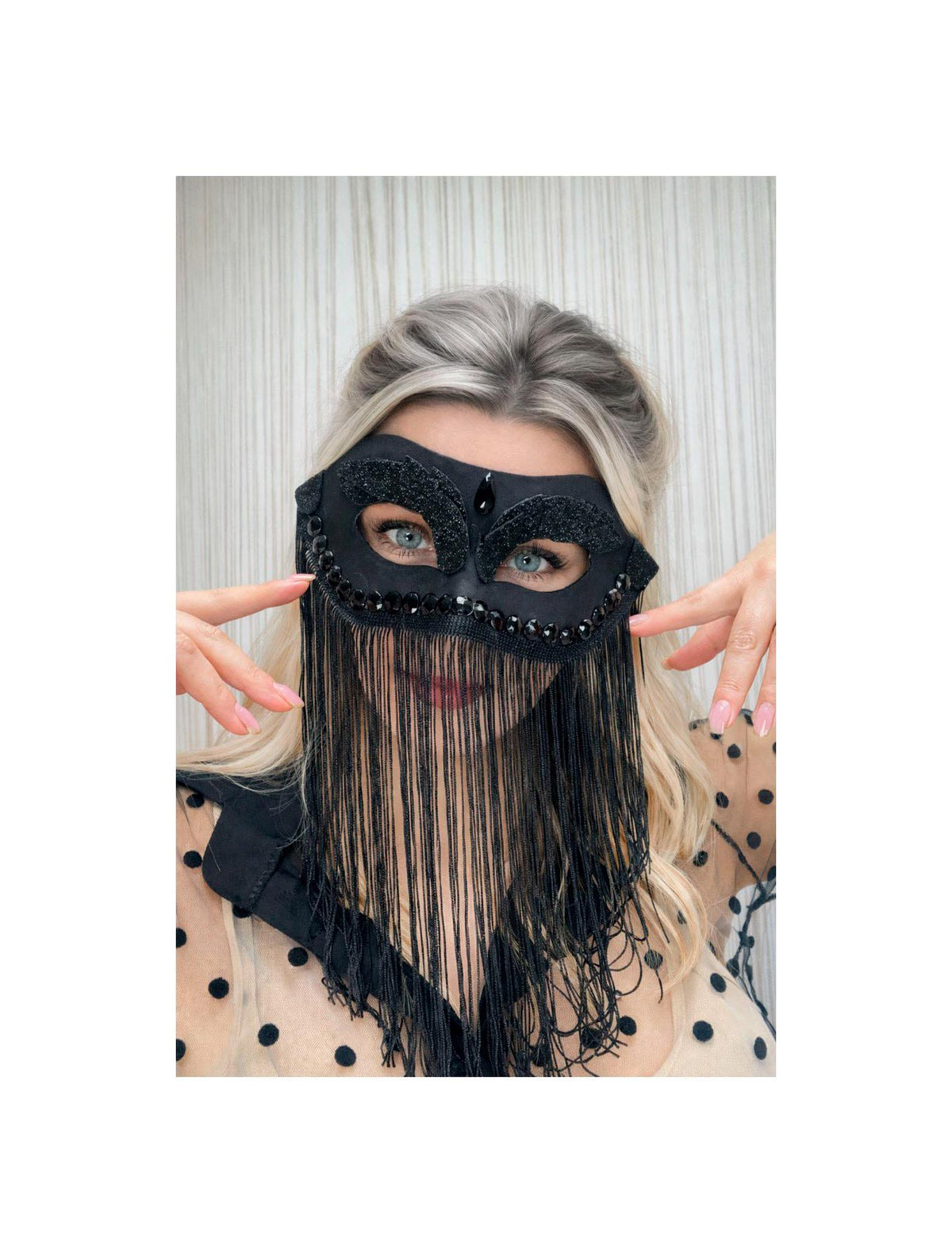 May include: Black masquerade mask with beaded and fringed details. The mask features a decorative design with embellishments around the eye openings and a fringe that hangs down. The mask is made of a soft, dark material.