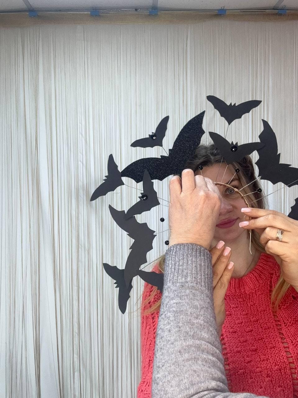 May include: A Halloween-themed headpiece featuring black bat cutouts. The bats are arranged in a circular pattern, with some having glitter accents. The headpiece is being held in place, suggesting it's a costume or decorative item.
