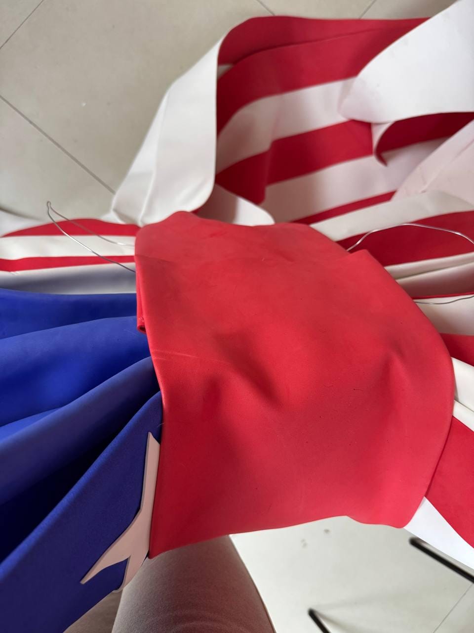 May include: A partially visible American flag, with red and white stripes and a blue field with a white star. The flag is made of fabric and appears to be in the process of being assembled or displayed.