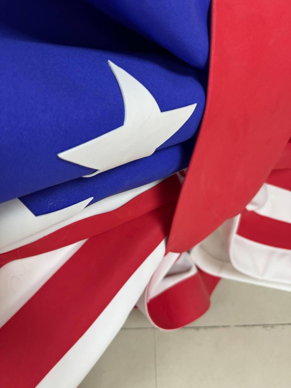 May include: Close-up of a folded American flag. The flag features a blue field with a white star, red and white stripes, and a red border. The flag is made of a lightweight fabric.