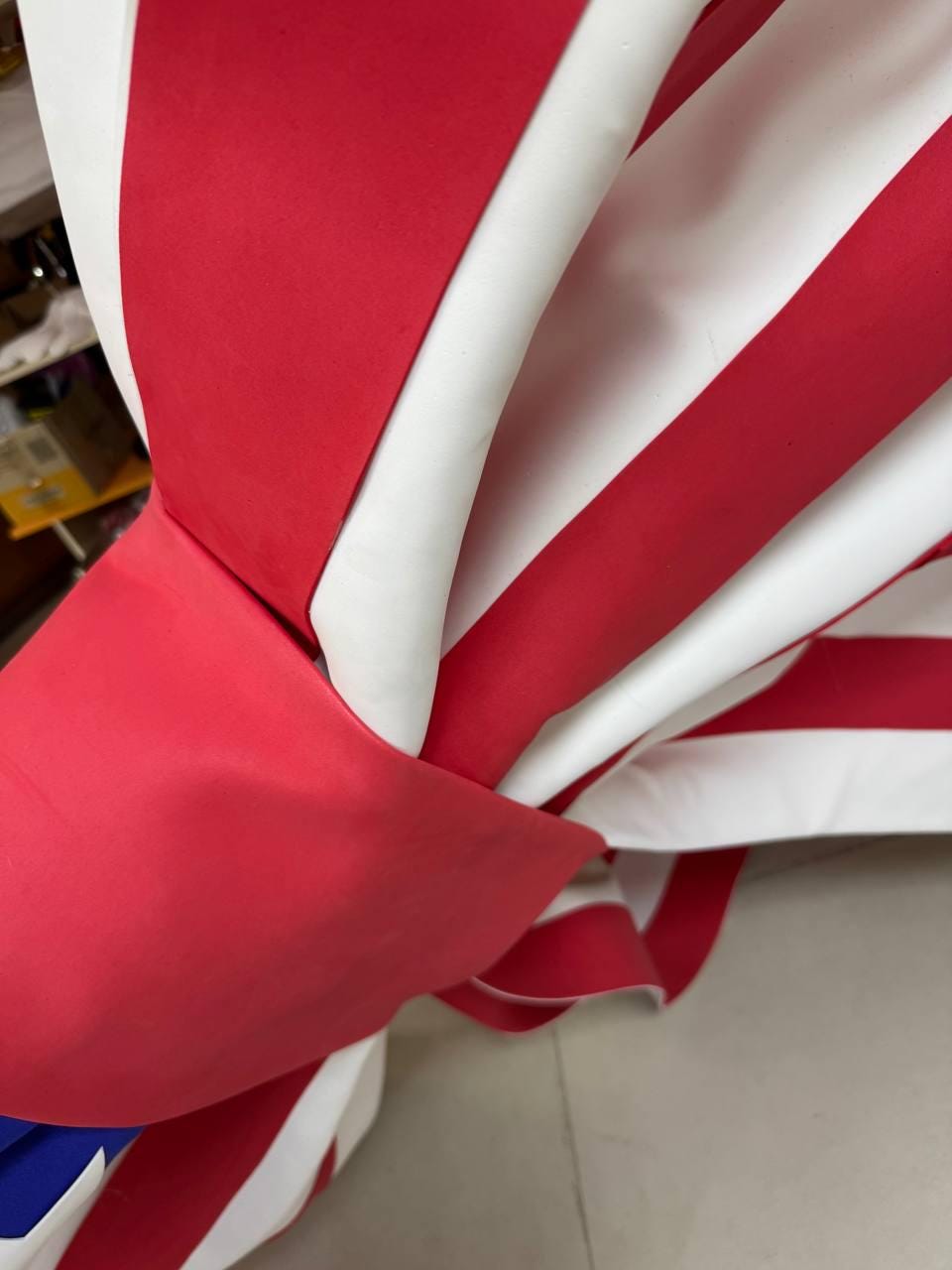 May include: Close-up of a red, white, and blue fabric, possibly a flag or decorative item. The fabric is folded and draped, with the red stripes prominently displayed. The white stripes and blue section are also visible.