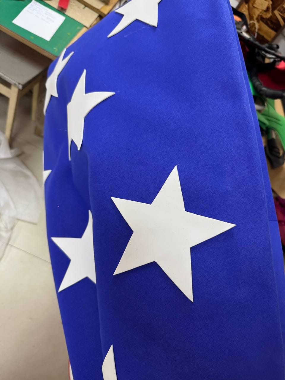 May include: Close-up of a blue fabric with white star cutouts. The stars are of varying sizes and are evenly spaced across the surface. The fabric appears to be a flag or banner.
