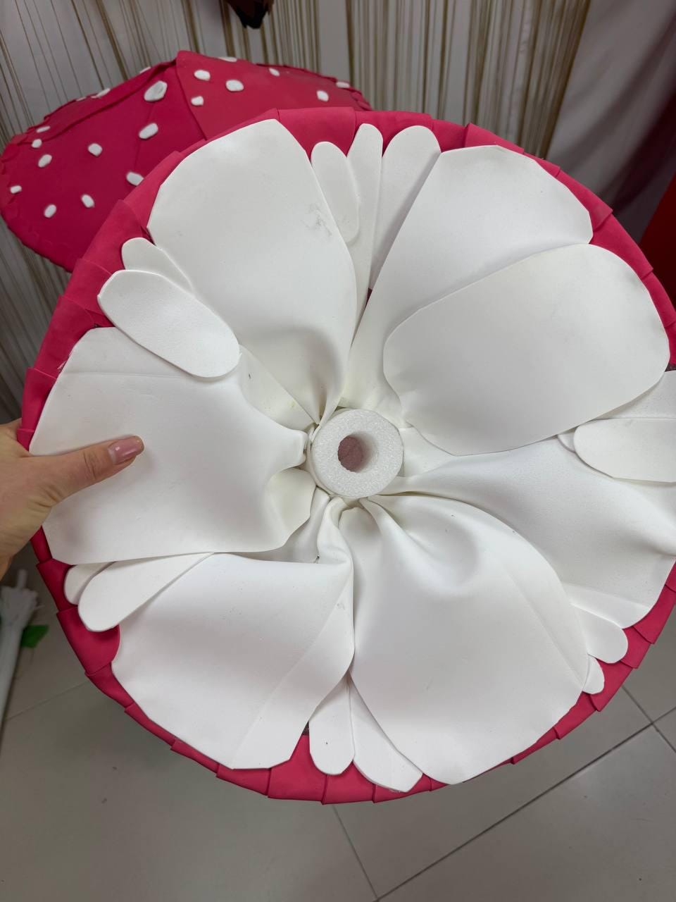 May include: A large, decorative mushroom-shaped object with a bright pink base and white petal-like accents. The top is a vibrant pink with white polka dots. The design is reminiscent of a whimsical, oversized flower.