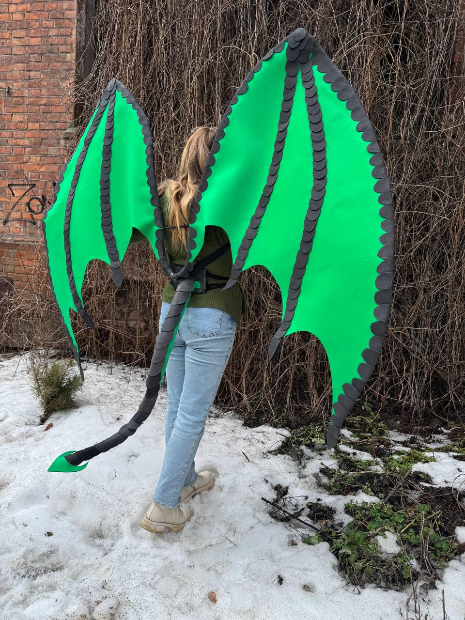 May include: Bright green dragon wings with black trim and a matching tail. The wings are large and spread out, with a scalloped edge. The tail is long and has a green tip. The wings are attached to a harness.