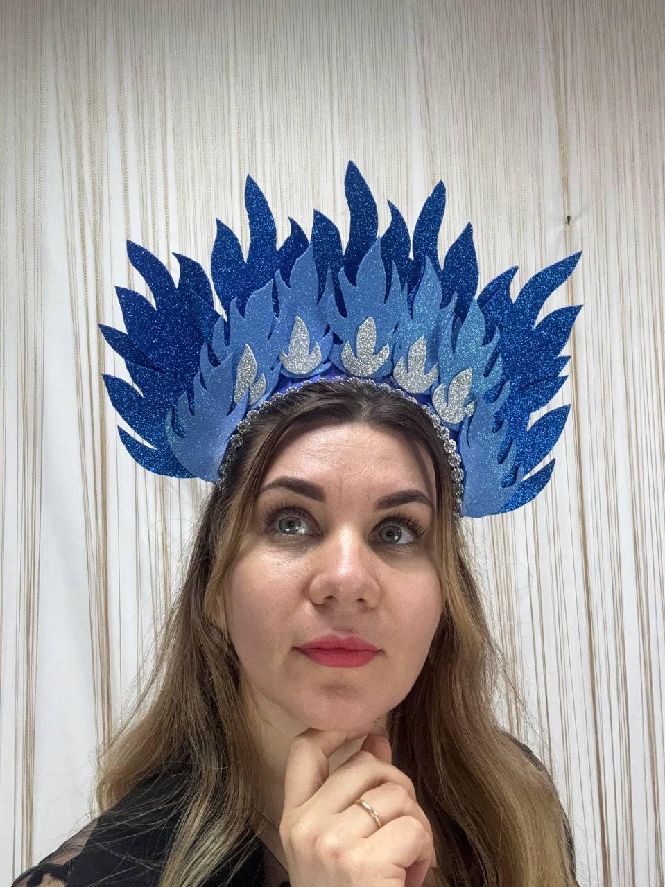 May include: A blue and silver glitter flame headdress. The headpiece features layered blue flame shapes with silver glitter accents and a beaded band. This festive headwear is suitable for cosplay or themed events.
