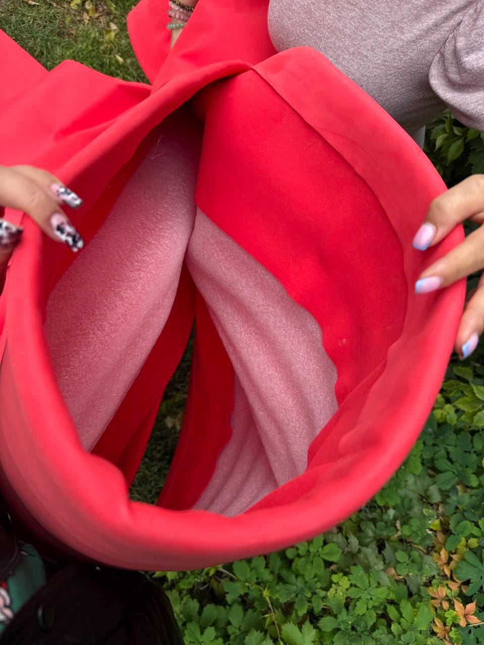 May include: A large, bright red fabric bow, possibly for gift wrapping or decoration. The bow is open, revealing a light pink interior. The image is taken from a close-up perspective, with hands visible on either side.