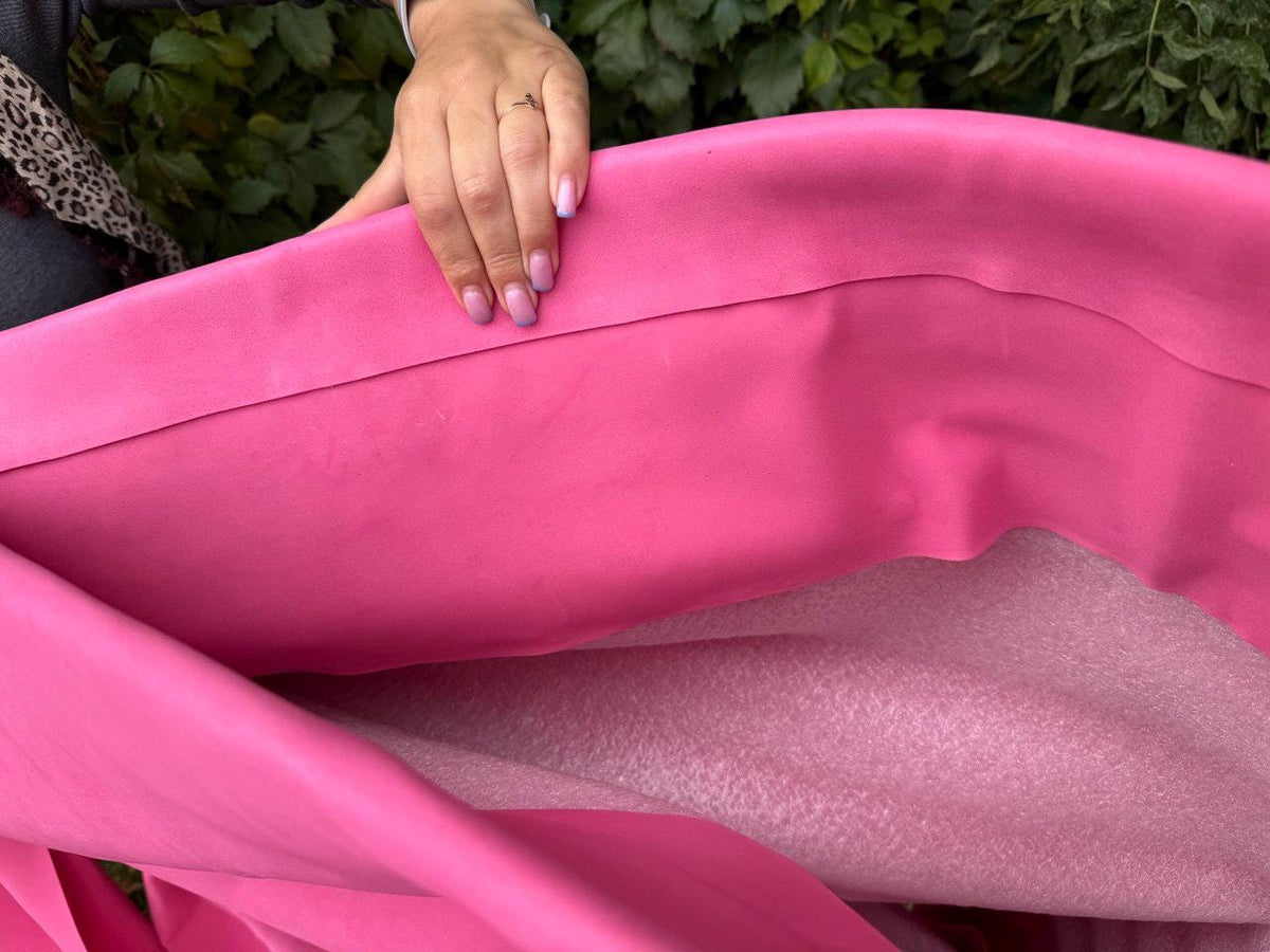 May include: A vibrant pink fabric, possibly leather or a similar material, is folded to reveal a lighter pink, textured layer beneath. The image showcases the material's smooth surface and color variation. The fabric is being held.