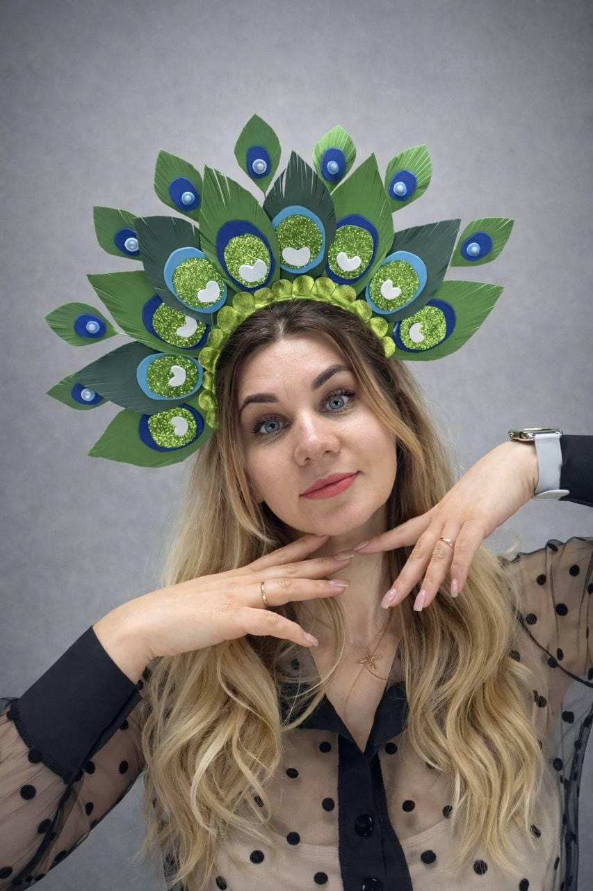 May include: A decorative peacock feather headpiece with green, blue, and white accents. The headpiece features large, stylized feathers with glitter details and is worn on the head. The design is vibrant and eye-catching.