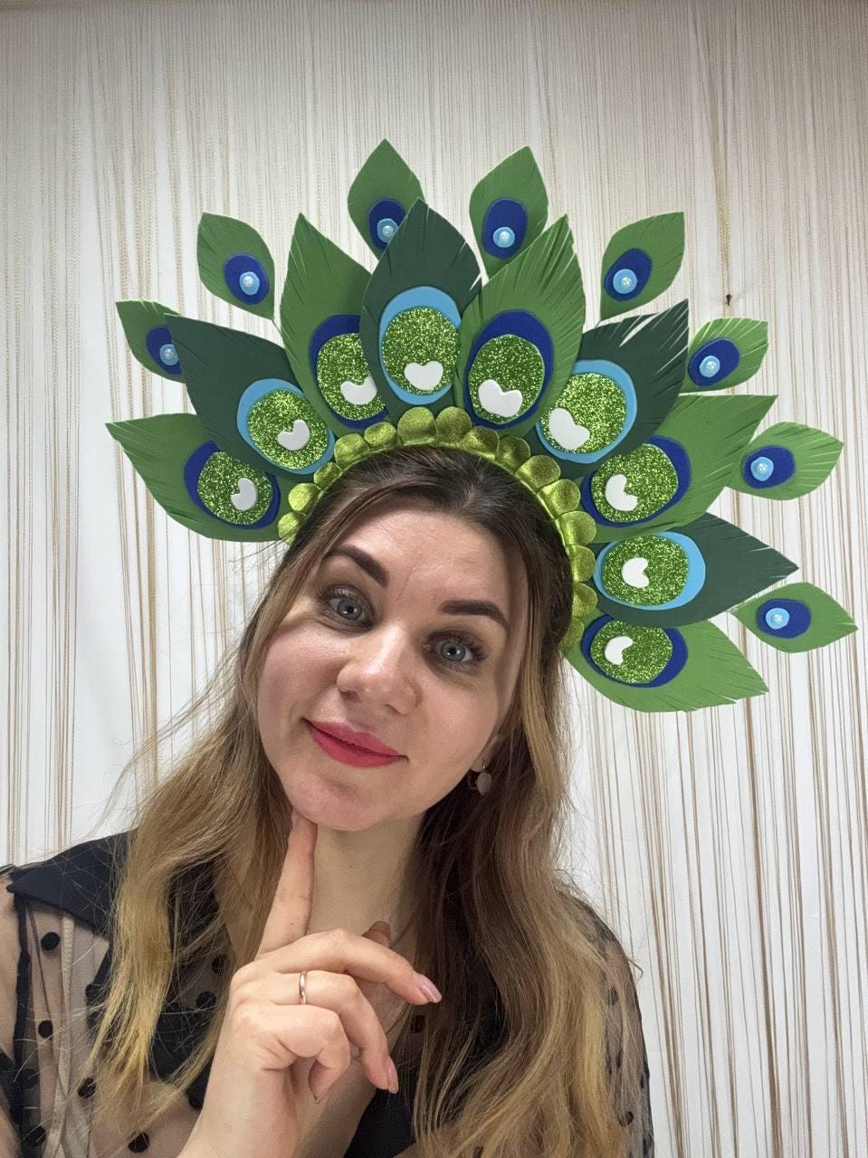 May include: A green and blue peacock feather headdress with glitter accents. The headpiece features large, stylized feathers in shades of green, blue, and white, creating a vibrant and eye-catching design. The base is a green headband.