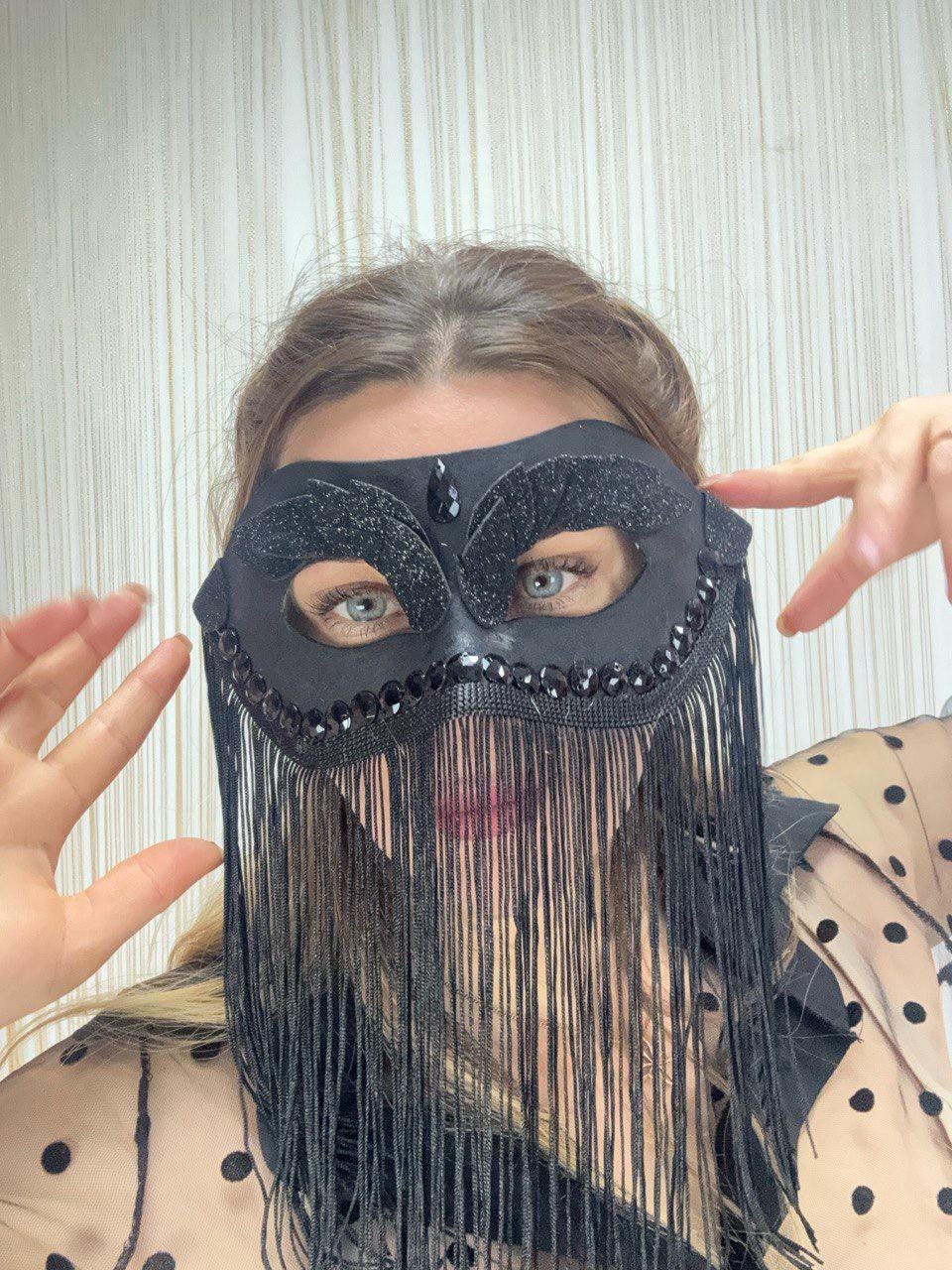 May include: Black eye mask with a decorative design, featuring a fringe and embellished with rhinestones. The mask has a glittery texture and is designed to cover the eyes and nose. The mask is suitable for masquerade balls or costume parties.