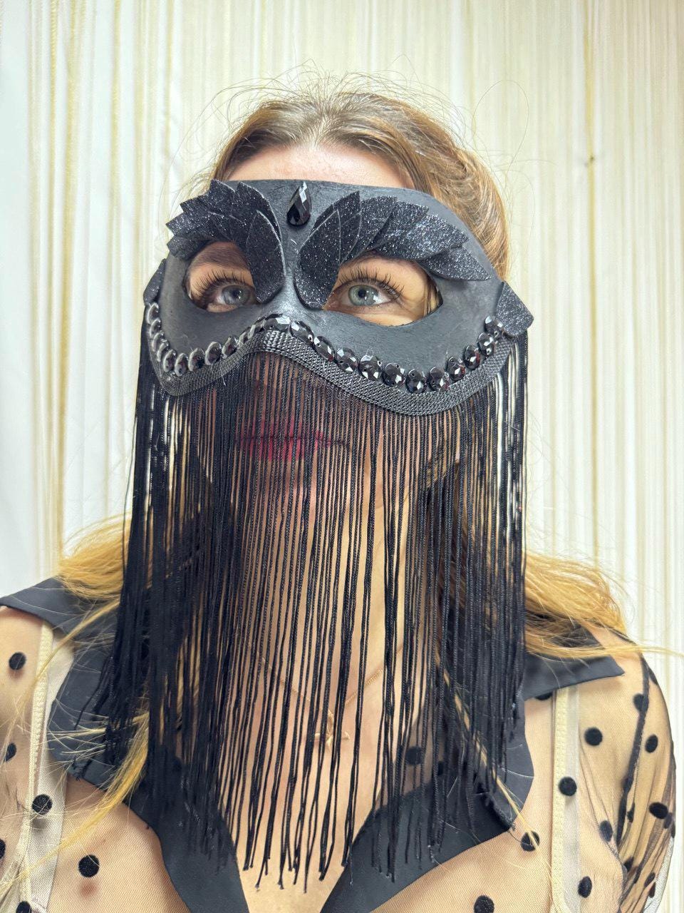 May include: A black masquerade mask with a decorative design. The mask features a central teardrop-shaped gem, embellished with black glitter and fringe. The mask is designed to cover the eyes and forehead.