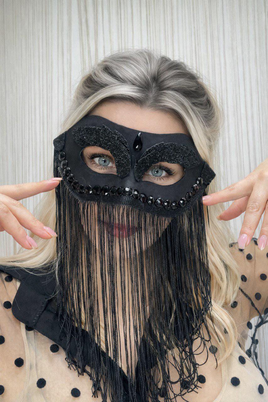 May include: Black masquerade mask with a decorative design and fringe. The mask features a sparkling embellishment around the eye openings and a teardrop-shaped jewel. The fringe hangs down, partially obscuring the lower face.