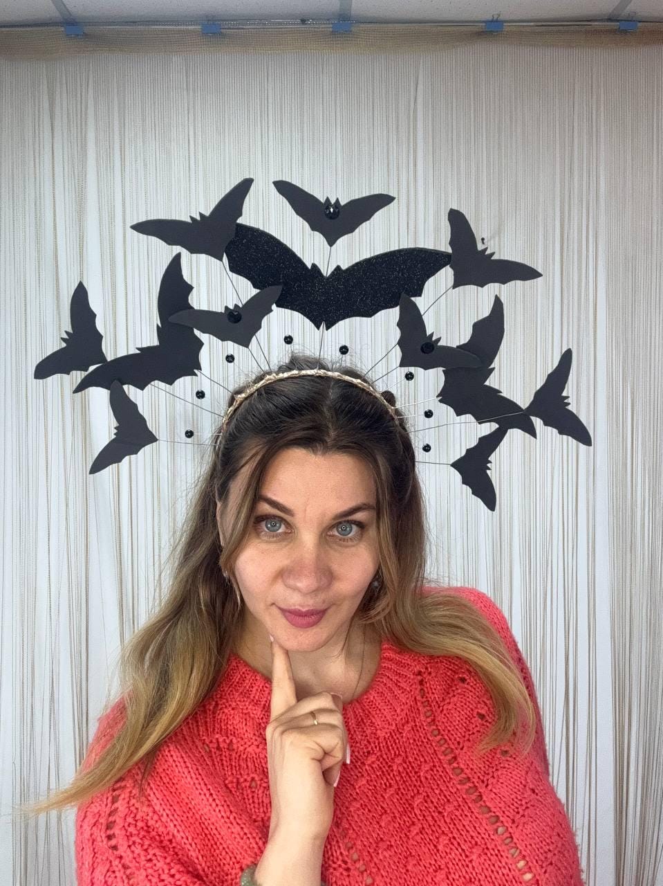 May include: A Halloween-themed headpiece featuring a gold-colored headband with black bat silhouettes. The bats are arranged in a decorative pattern, with a large glittery bat in the center. The headpiece is designed for festive occasions.