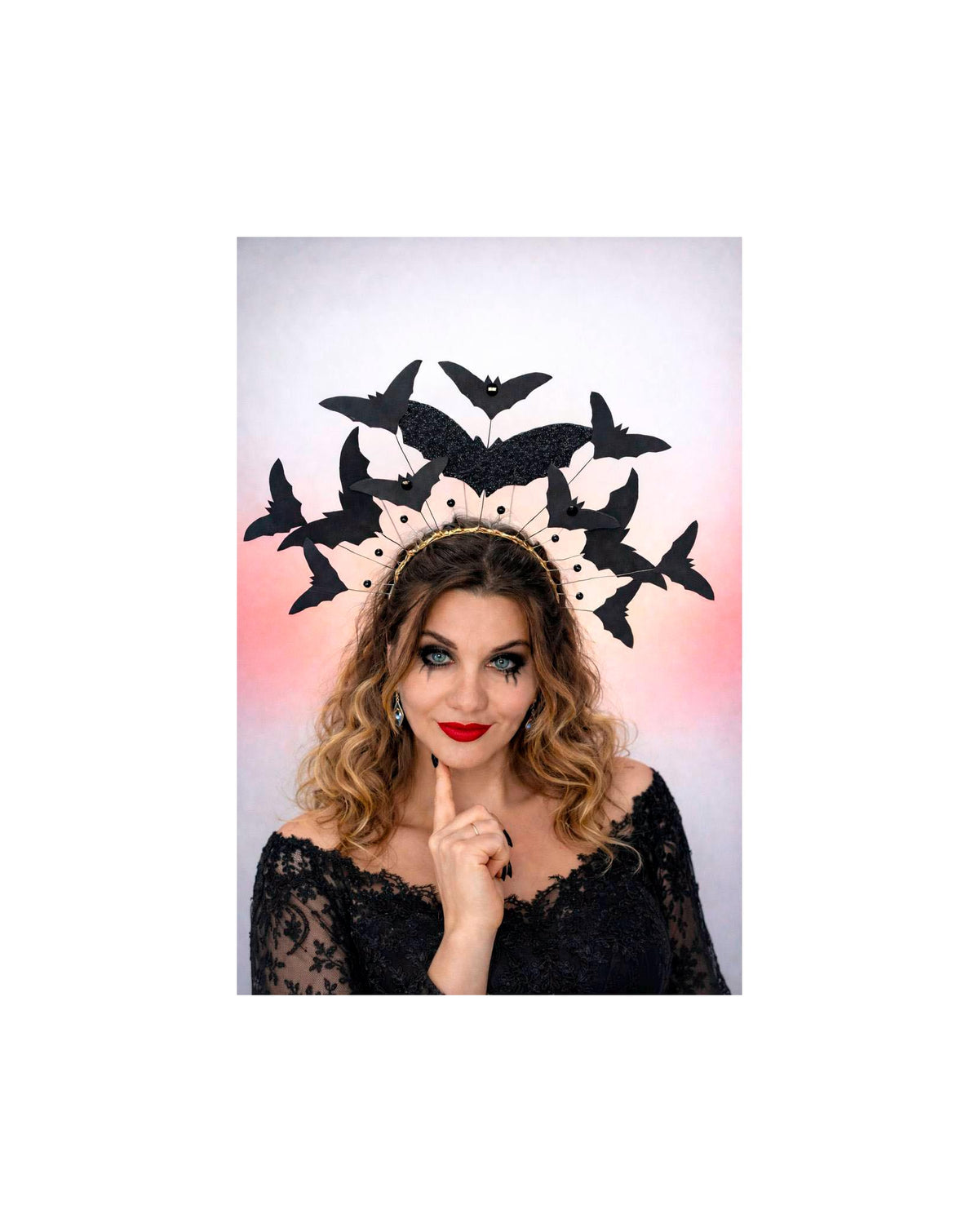 May include: A black bat-themed headpiece with a gold band. The headpiece features multiple black bat cutouts in various sizes. The woman in the image is wearing a black lace top and red lipstick, with dark eye makeup.