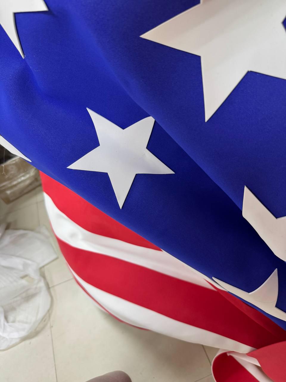 May include: Close-up of a draped American flag. The flag features a blue field with white stars and red and white stripes. The fabric is folded, creating shadows and texture.