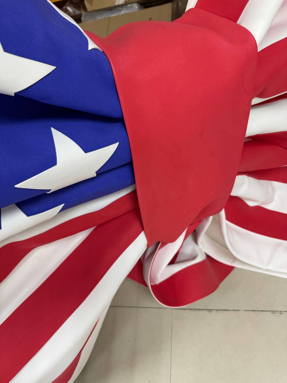May include: Close-up of a folded American flag. The flag features red and white stripes and a blue field with white stars. A red fabric is wrapped around the flag.