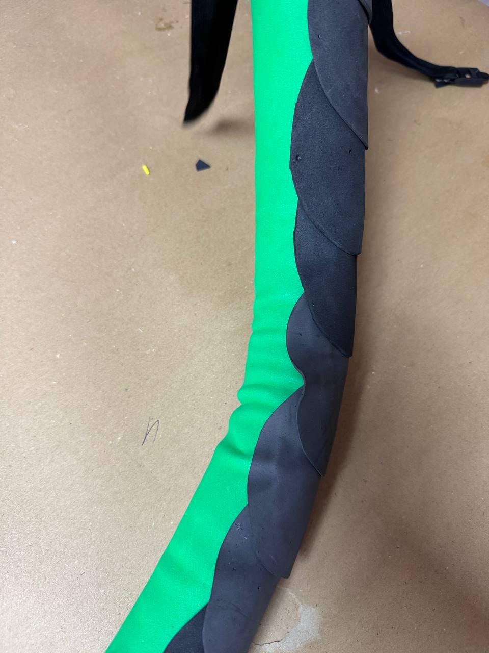 May include: A curved, green and black foam object. The green section is smooth, while the black section has a layered, scale-like design. The object is set against a neutral background.