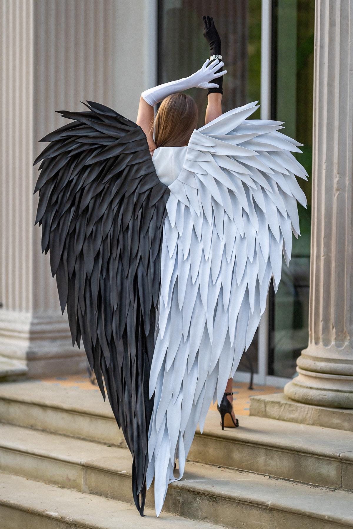 May include: Large decorative wings featuring a split design with one side composed of solid black feathers and the other side composed of solid white feathers. The wings are structured with layered, pointed feather-like segments extending outward.