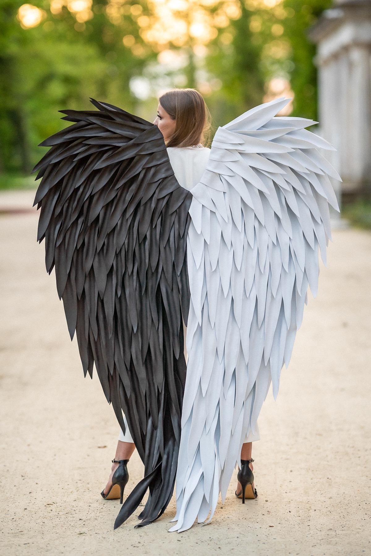 May include: A pair of large decorative wings featuring a split design with one side composed of black feathers and the other side composed of white feathers. The wings are structured with layered, pointed feather-like elements in a dual-tone color scheme.