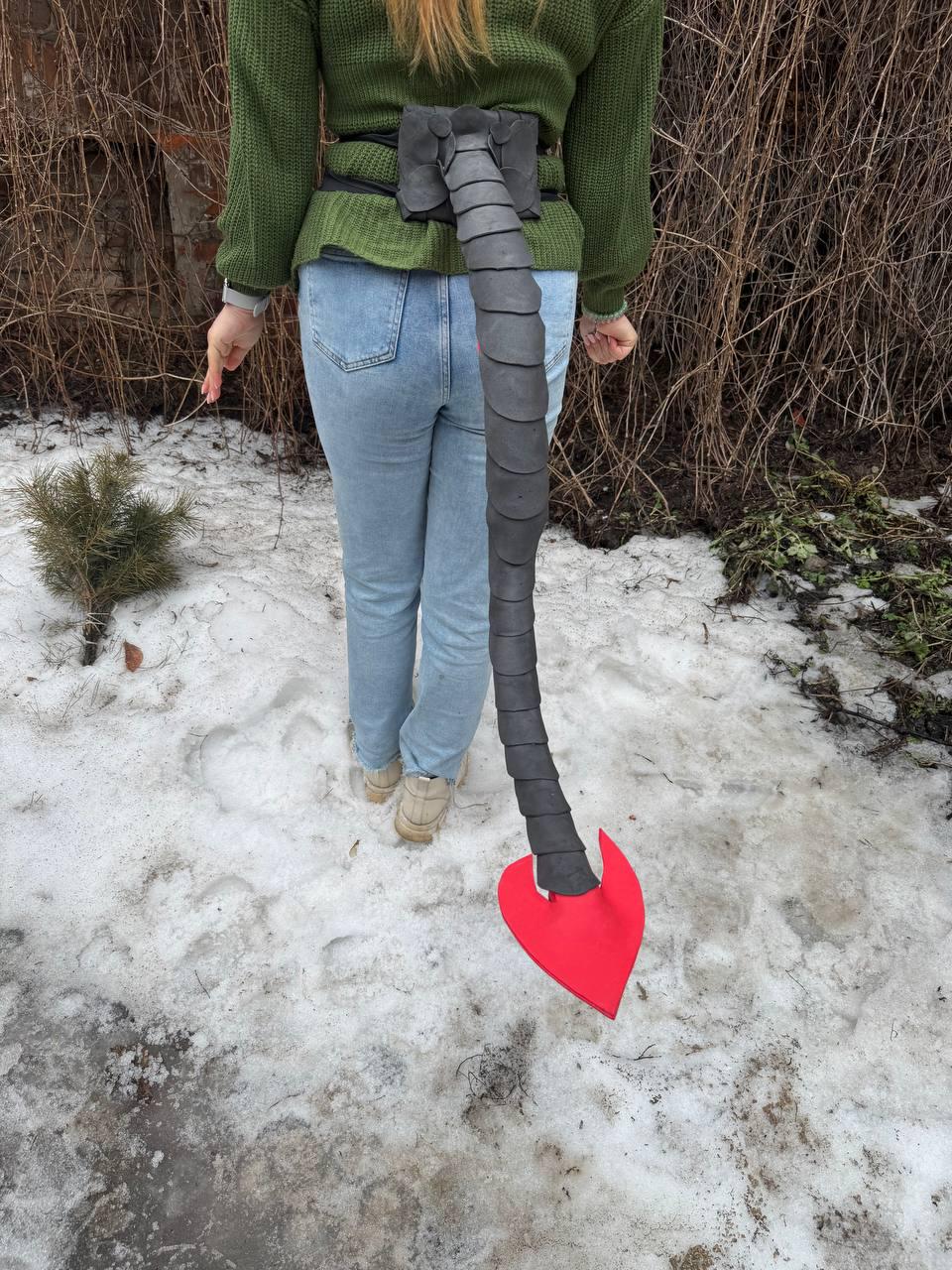 May include: A costume tail, black with a red heart-shaped tip, attached to a black belt. The tail is segmented and appears to be made of a flexible material. The belt is worn around the waist.