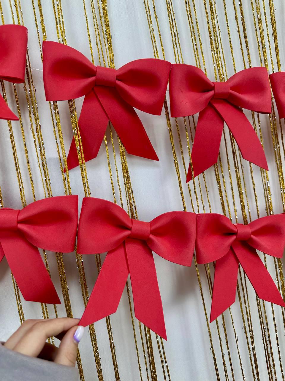 May include: A collection of vibrant red bows, each with a classic bow shape and long, flowing tails. The bows are arranged in a row against a backdrop of gold, shimmering strands, creating a festive and decorative display.