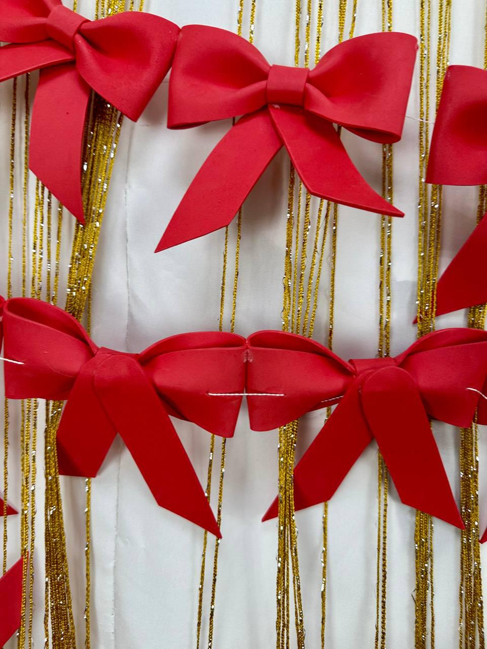 May include: Bright red bows are arranged against a backdrop of gold strands and a white surface. The bows are made of a smooth material and are tied in a classic bow shape. The gold strands add a touch of sparkle.