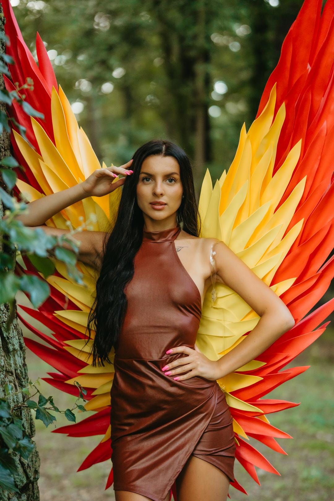 May include: Large, vibrant wings featuring layered, pointed feathers in shades of bright yellow, orange, and red. The wings are designed to be worn on the back, with a structure that fans out behind the shoulders, creating a bold, colorful display.