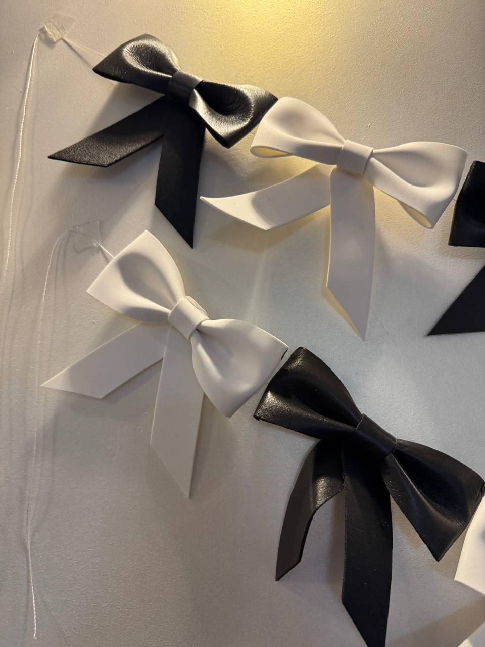 May include: Black and white bow decorations. The bows are made of a smooth material and are arranged in a row. The bows are attached to a white surface with a thin string.