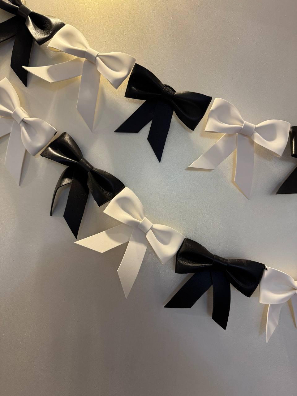 May include: Rows of black and white bows are arranged against a neutral background. The bows are made of a smooth material and are evenly spaced. The bows are a classic decorative element.
