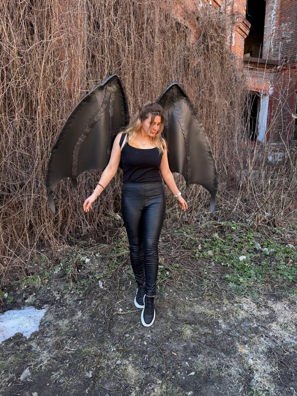 May include: A pair of large, dark gray dragon wings with a textured, scale-like pattern along the edges. The wings are attached to a black tank top worn with black leggings and black sneakers, creating a cohesive dark-toned ensemble.