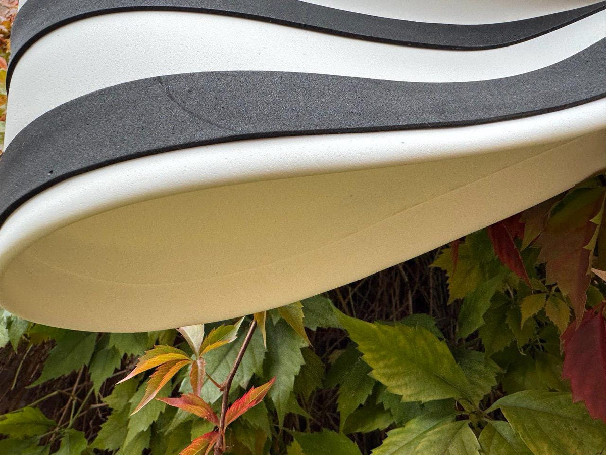 May include: Close-up of a white and black striped object with a curved design. The object has a smooth, glossy finish and appears to be made of a durable material. The background features green and red leaves.
