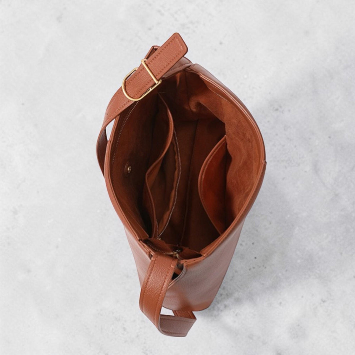 May include: A brown leather shoulder bag with an open top, revealing multiple interior pockets. The bag has a long strap with a gold-colored buckle and a smaller handle. The interior is a lighter shade of brown than the exterior.