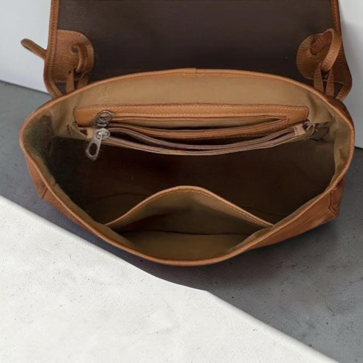 May include: Open view of a brown leather satchel bag. The bag has a flap closure and a spacious interior with multiple pockets. The interior lining is a lighter shade of brown. The bag appears to be made of high-quality leather.