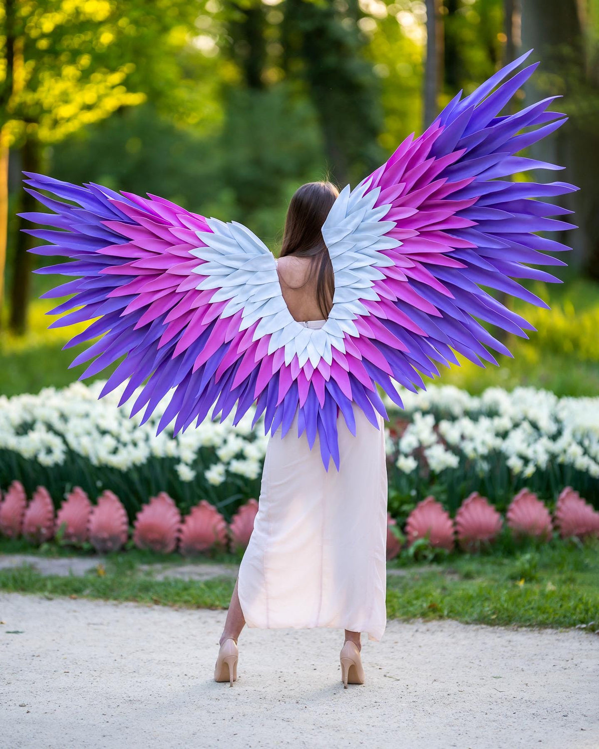 May include: Large decorative wings featuring a layered feather design in a gradient of white, pink, and purple. The wings are constructed with individual pointed segments that fan out widely, creating a textured appearance across the entire span.