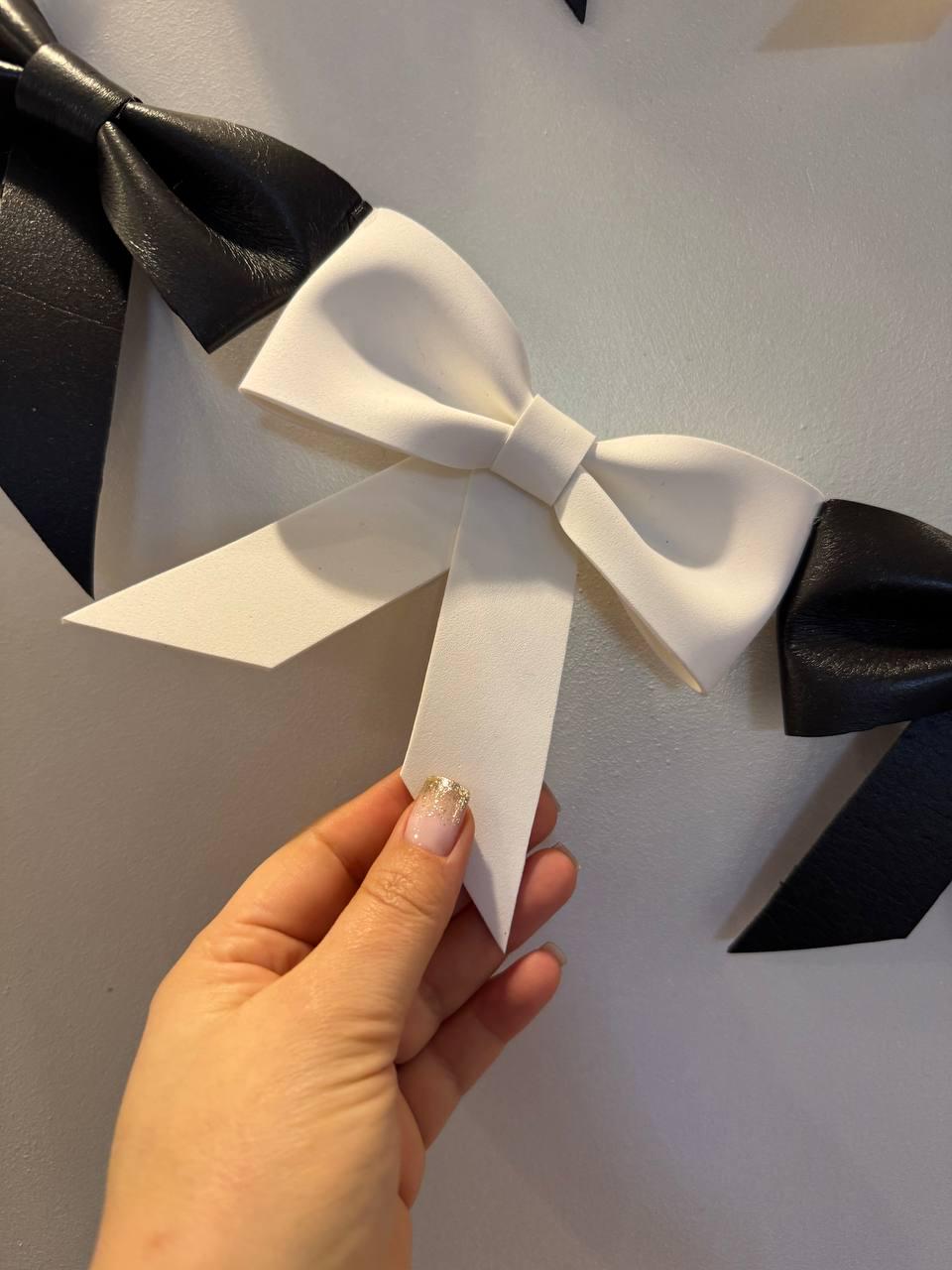 May include: A series of black and white decorative bows. The bows are made of a leather-like material. One hand is holding a white bow. The bows are attached to a wall. The bows are a decorative element.