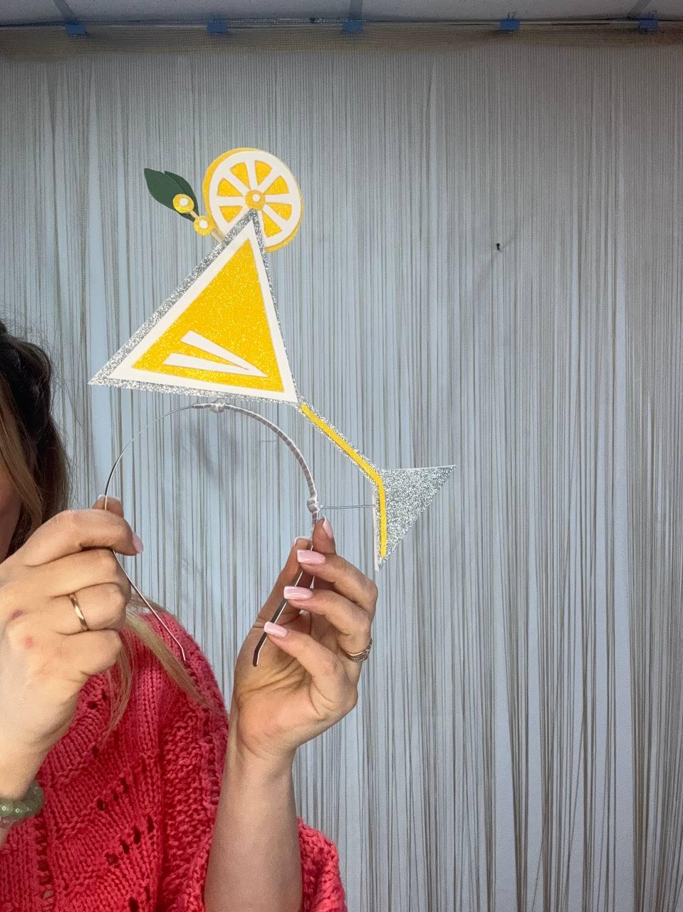 May include: A yellow and silver martini-shaped headband with a lemon slice detail. The headband features a triangle-shaped cocktail glass with silver glitter accents and a yellow stem. The lemon slice has white and yellow segments with a green leaf.