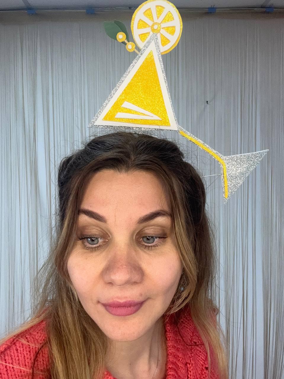 May include: A whimsical cocktail-themed headpiece featuring a yellow triangle and a silver glitter accent. The design includes a lemon slice and a long, thin silver glitter stem. The headpiece is a fun accessory for parties or events.