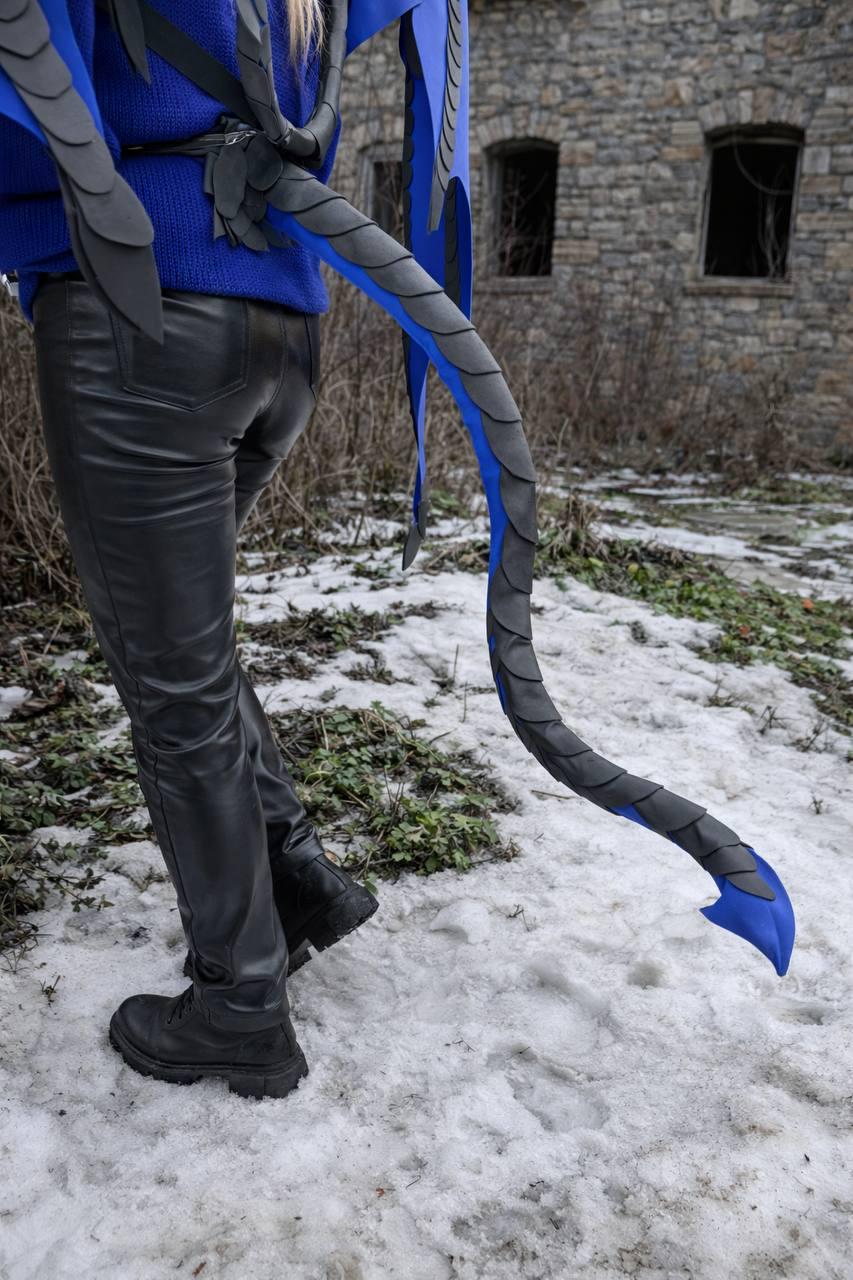 May include: A blue and black dragon tail costume with a matching back piece. The tail is long and curved, with a blue underside and black scales. The costume is worn with black pants and boots.