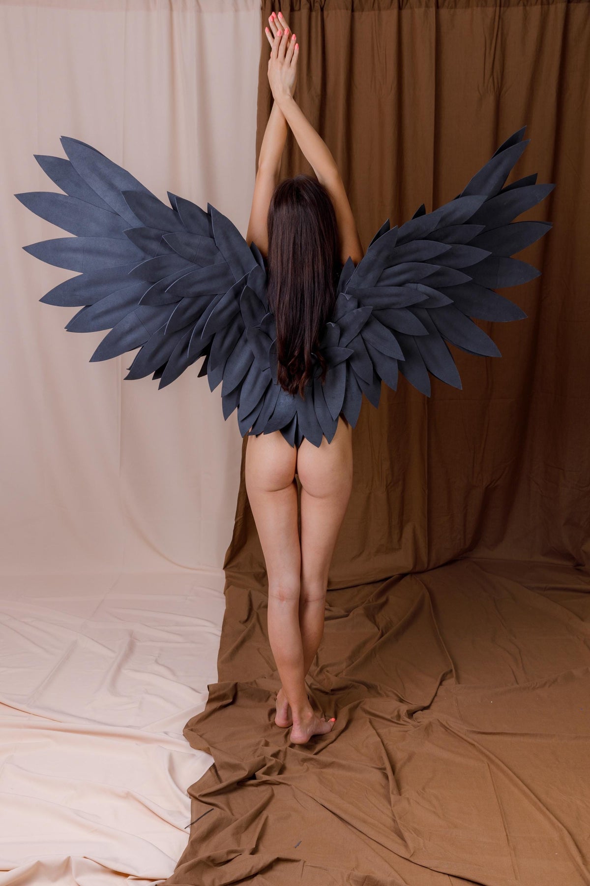 May include: A pair of large, dark gray, feathered wings constructed with layered, pointed, leaf-shaped elements. The wings are expansive and span horizontally, featuring a matte texture and a structured design that mimics the appearance of bird wings.