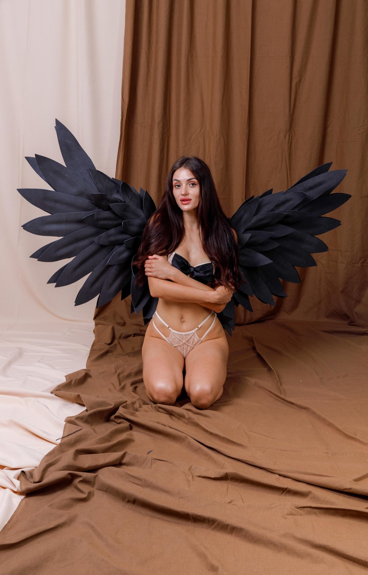 May include: Large, articulated black wings with layered, feather-like panels attached to a harness. The wings feature a wide, expansive span with pointed tips, constructed from a matte black material, designed to be worn on the back for costume use.
