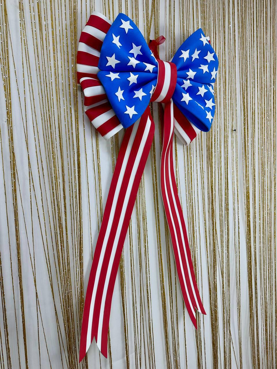 May include: A patriotic bow featuring a blue center adorned with white stars, and red and white striped accents. The bow has long, red and white striped streamers. This decorative bow is perfect for Independence Day or other patriotic celebrations.